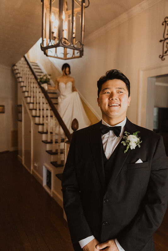 bride walking down steps behind groom for first look in farmhouse