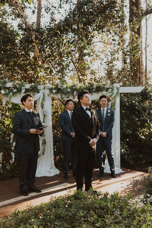 groom standing at altar with greenery and wisteria