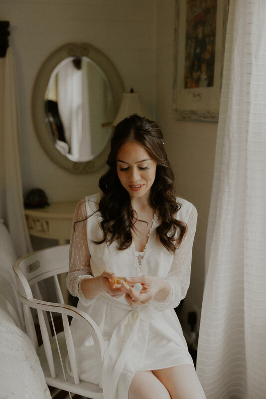 bride in getting ready robe putting on perfume