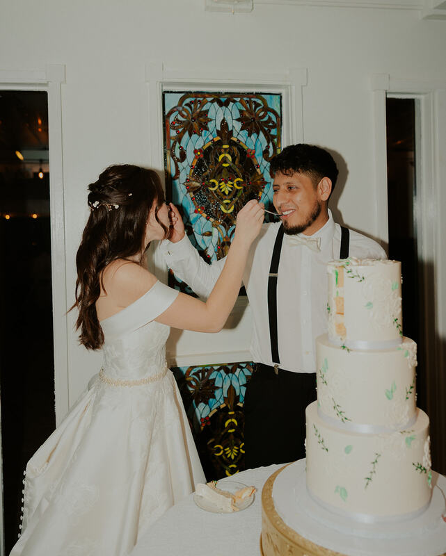 newlyweds feeding each other cake by stained glass window