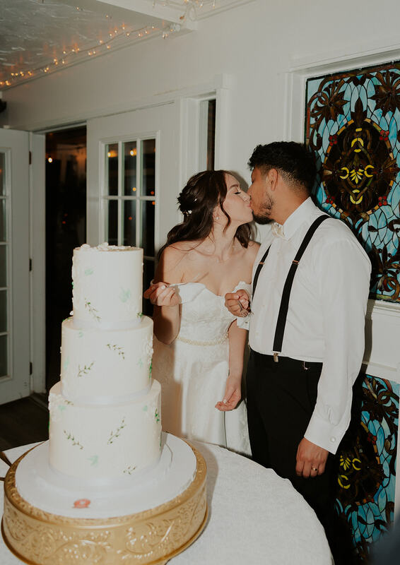 bride and groom kissing by 3-tier white cake with simple greenery frosted design