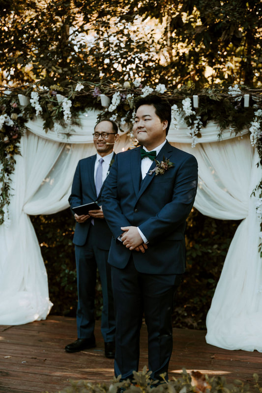 groom standing at altar with dramatic drapes and florals