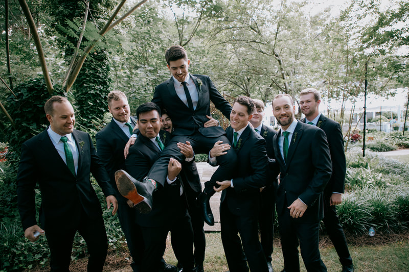 groomsmen in black suits with green ties holding up groom
