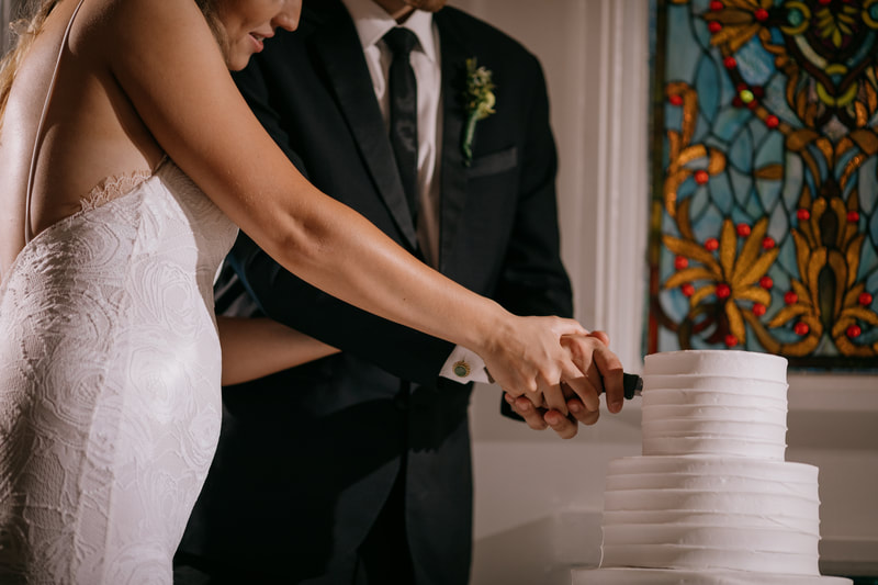 newlyweds cutting all-white 3-tiered wedding cake
