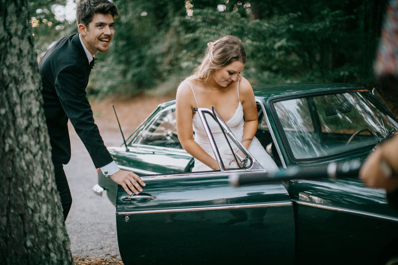 groom helping bride into vintage car for sendoff
