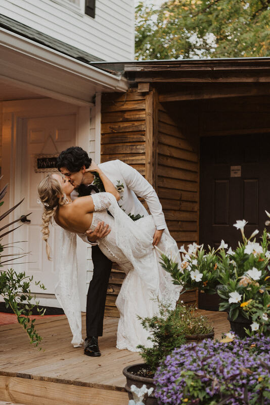 groom dips bride for kiss on farmhouse porch
