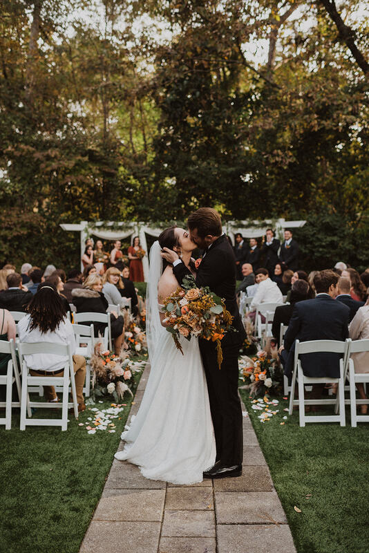 newlyweds kissing at end of outdoor boho fall ceremony site