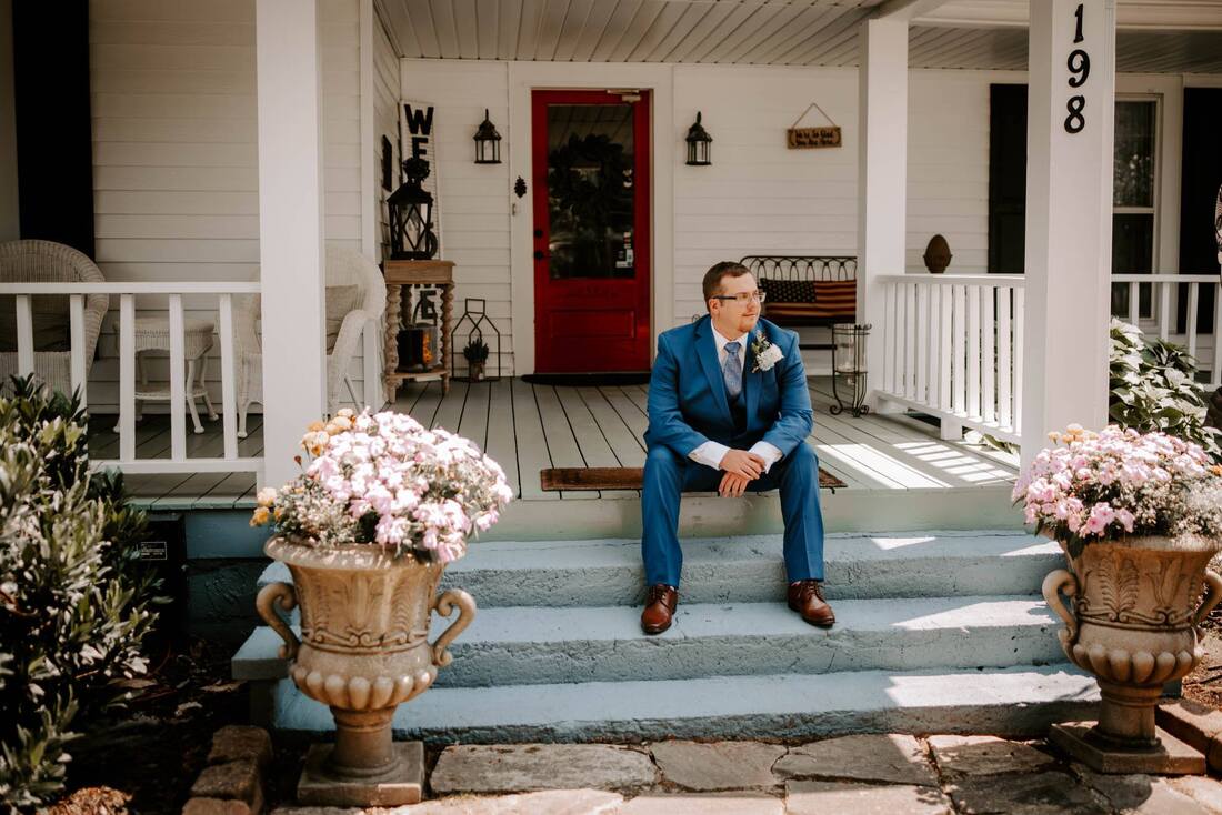 groom in navy suit sitting on farmhouse steps