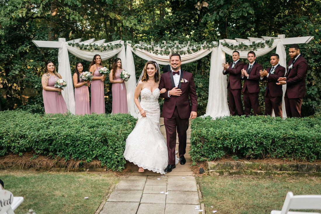 newlyweds and bridal party by altar with blush and wine colored outfits