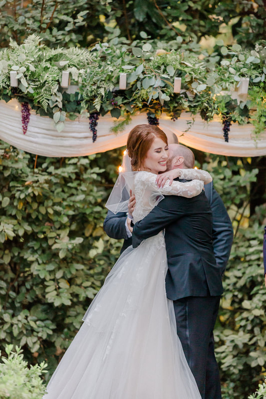 bride and groom hugging at altar decorated with hanging grapes