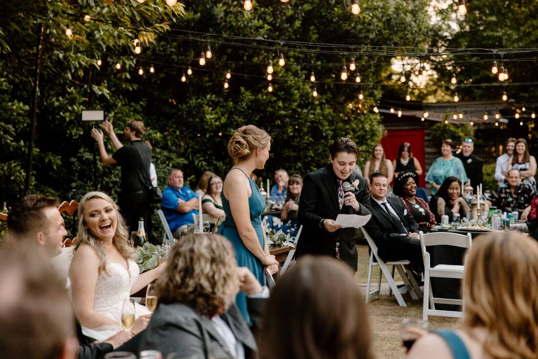 guests and bride laughing during toasts at garden reception