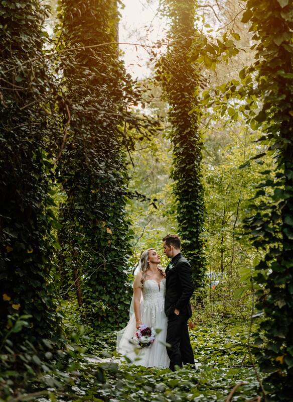 groom and bride standing in midst of ivy covered trees