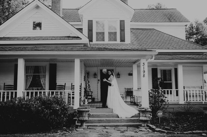 black and white photo of bride and groom posing on farmhouse porch steps