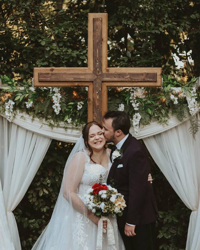 newlyweds in front of garden wedding arbor with a wooden cross