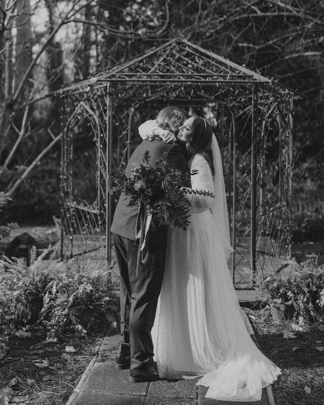 black and white photo of bride and groom hugging by garden gazebo