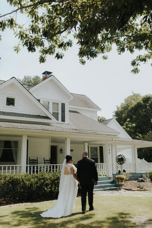 bride and groom walking toward white farmhouse venue