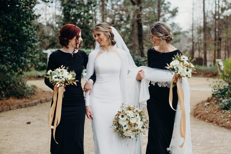 bride and bridesmaids walking through garden holding bouquets with champagne ribbons