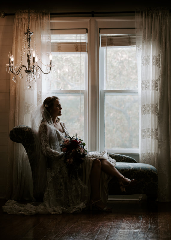 moody photo of bride sitting on chaise lounge by farmhouse window