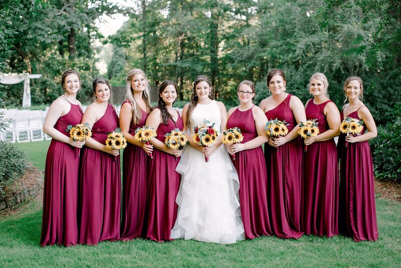 bride surrounded by bridesmaids in wine colored dresses all holding bouquets of sunflowers