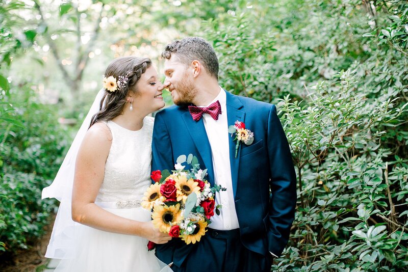 bride with sunflower in hair leans in to kiss groom in Four Oaks' gardens