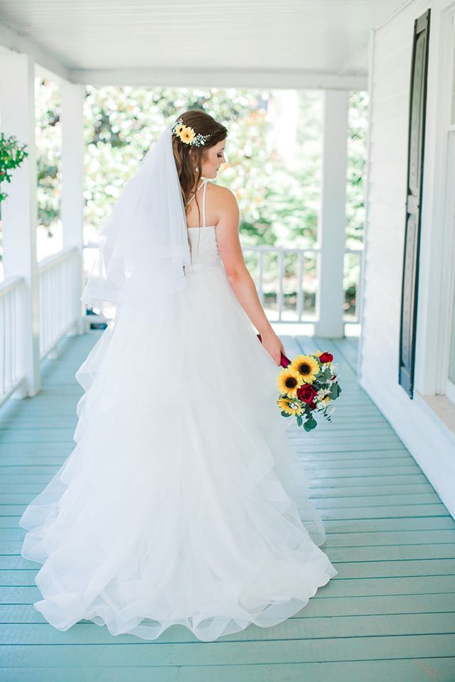 bride holds bouquet of sunflowers, red roses, baby's' breath, and eucalyptus leaves on farmhouse porch