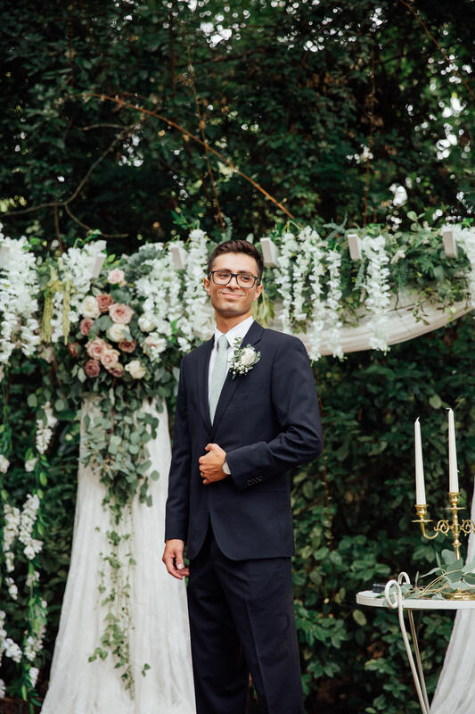 groom at altar decorated with full greenery and white and blush flowers