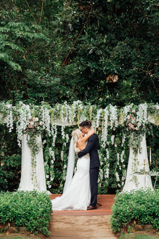 newlyweds kissing by altar decorated with greenery and white flowers