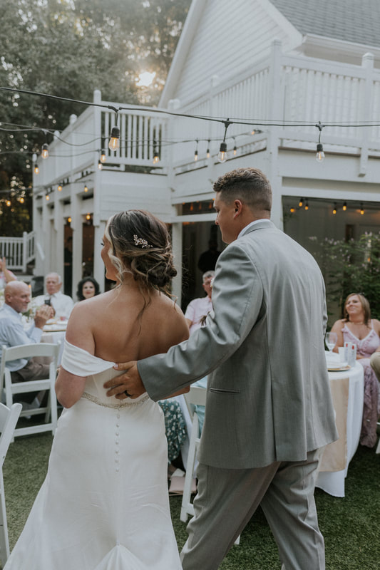 newlyweds walking through backyard reception with groom's hand on bride's back