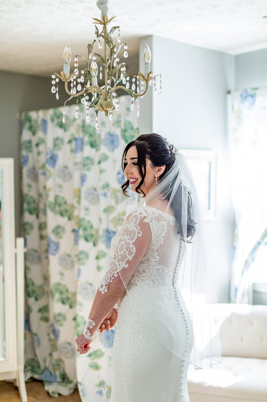 bride in lace dress and veil smiling while looking in mirror in bridal suite bathroom