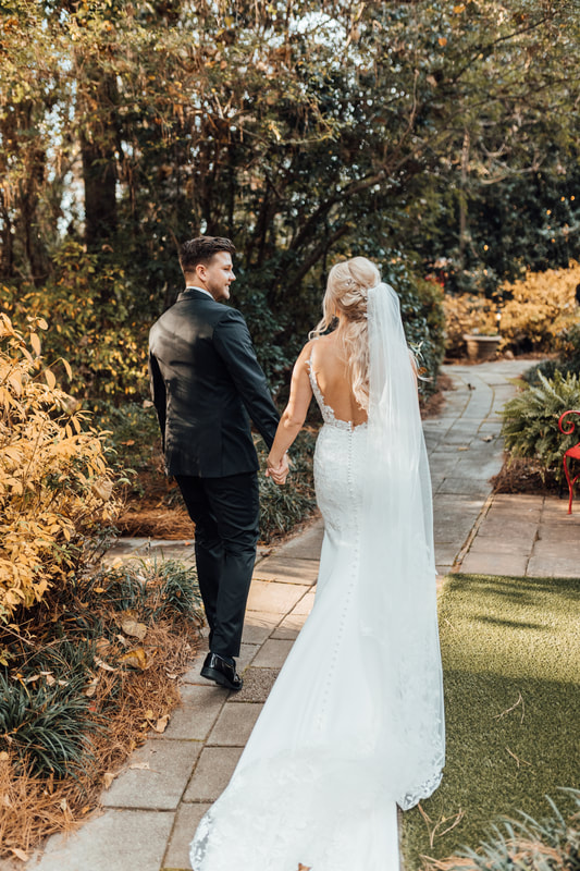 bride and groom walking through garden path holding hands