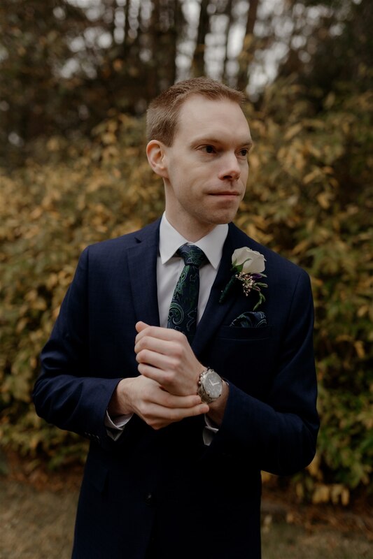 groom standing in four oaks manor's gardens and fixing watch