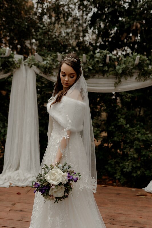 bride in fax fur warp standing at outdoor altar