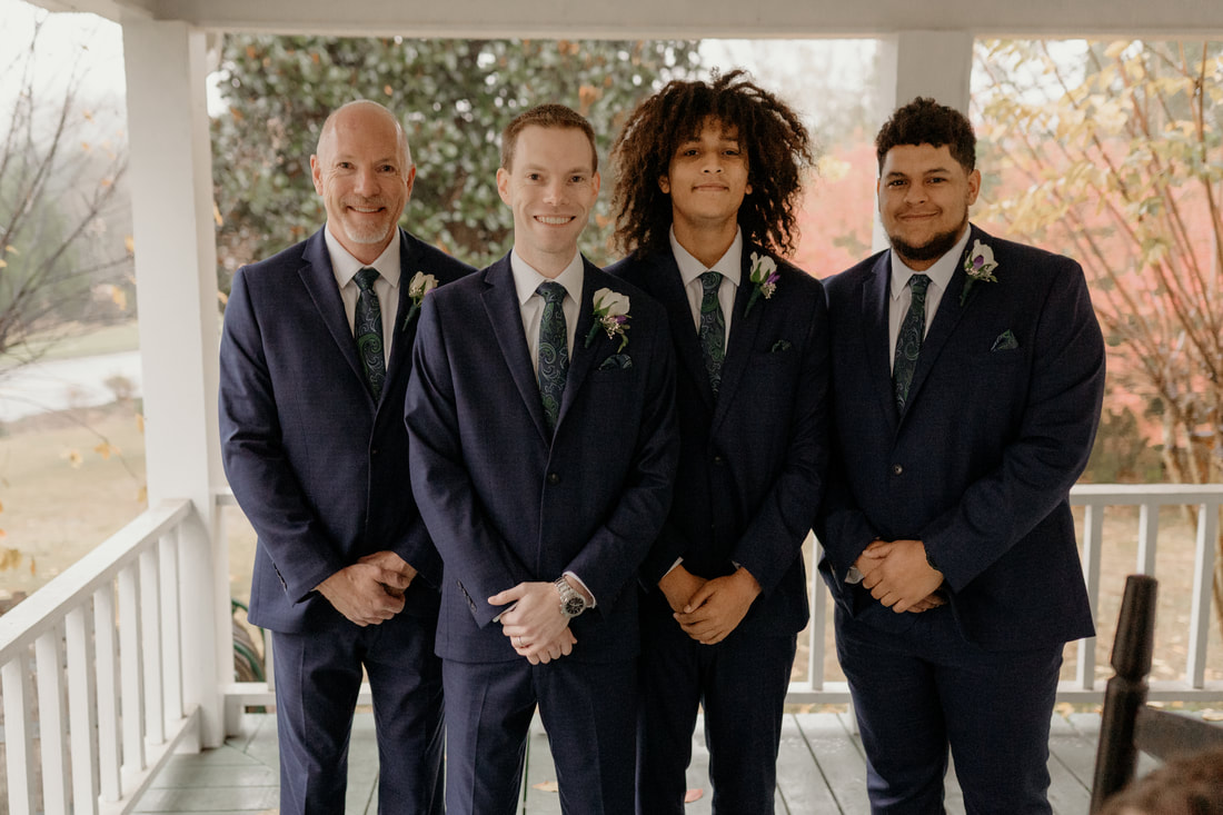 groom standing with groomsmen in matching suits on farmhouse porch