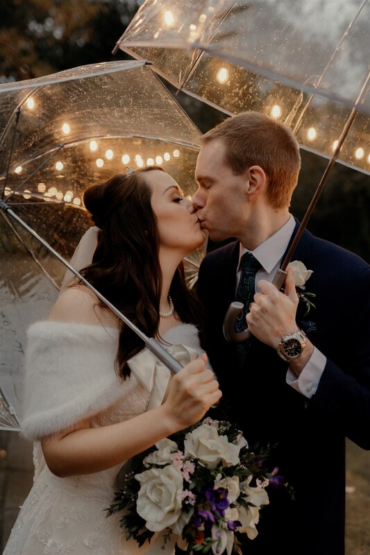 bride and groom kissing while holding umbrellas