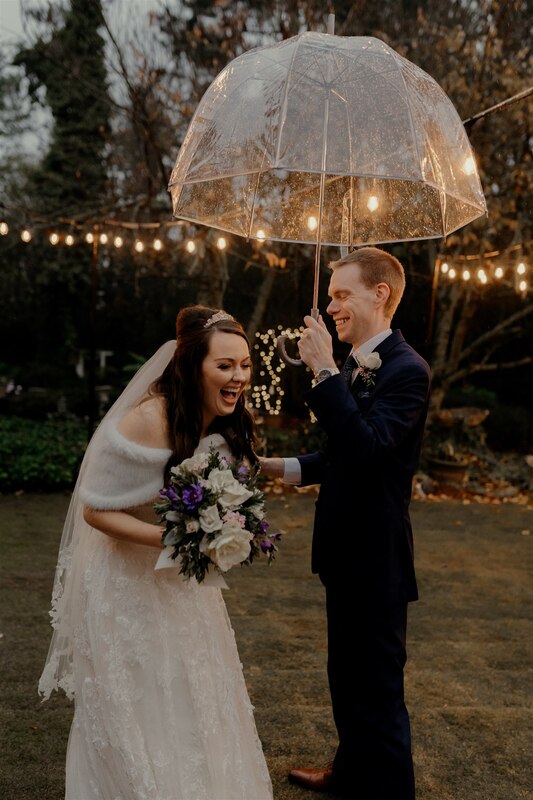 groom and bride laughing as groom holds clear umbrella