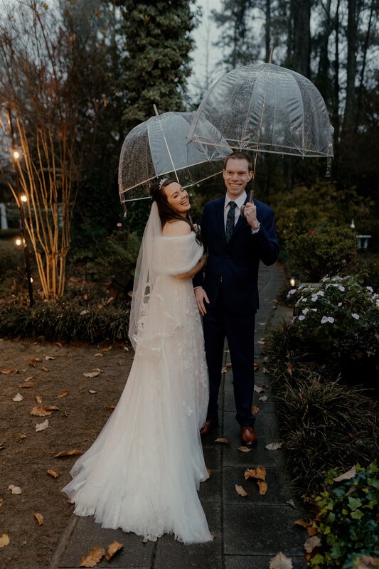 bride and groom standing in gardens with clear umbrella