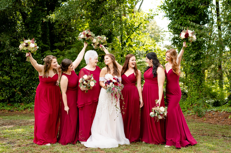 bridesmaids in burgundy dresses holding up bouquets with bride