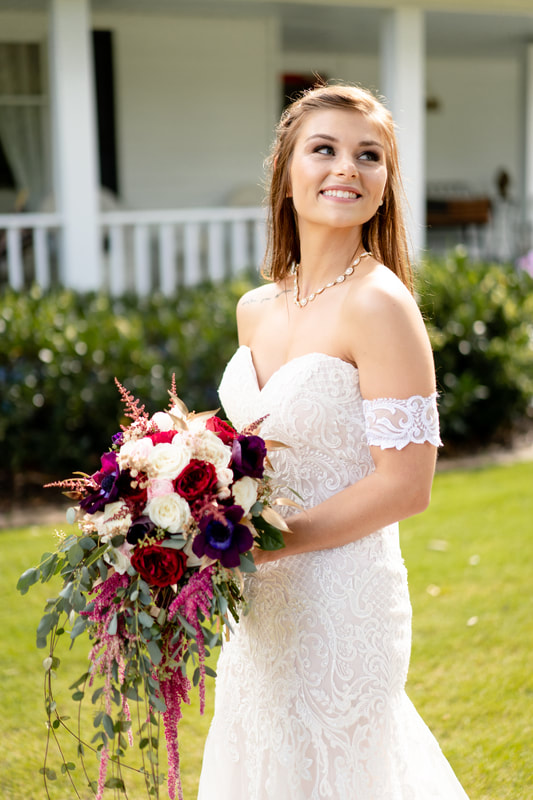 bride in lace dress holding purple, pink, and red bouquet