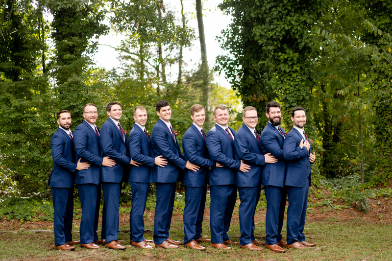 groomsmen in navy suits standing in line and holding each others' waists like a prom pose