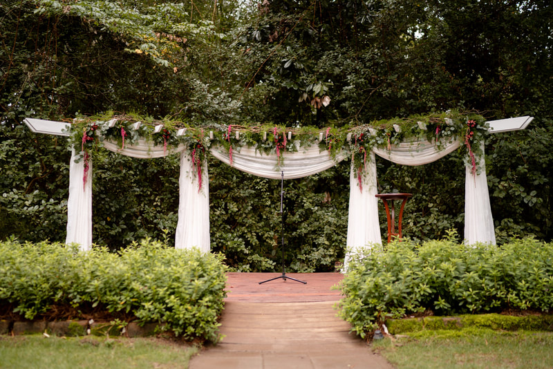 outdoor wedding altar decorated with white chiffon fabric, amaranth bunches, eucalyptus, fern leaves, and other greenery