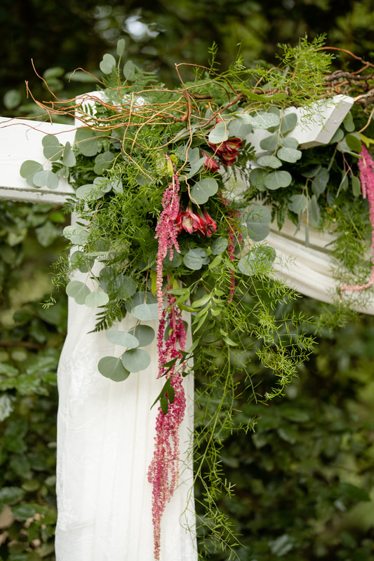 post of wedding altar decorated with eucalyptus, fern leaves, other greenery, Peruvian lilies, and amaranth