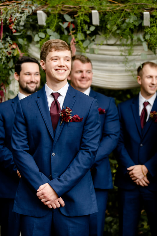 groom in blue suit smiles at bride walking down aisle