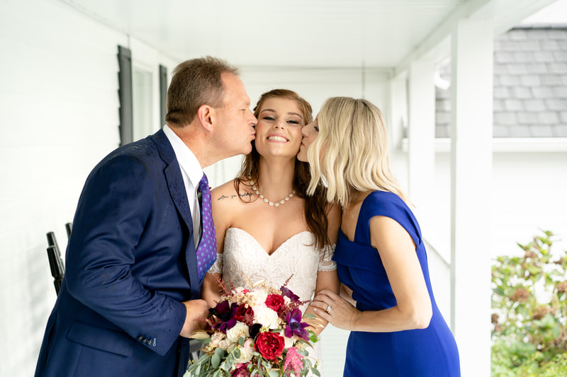 brides' parents kissing her cheek on farmhouse porch