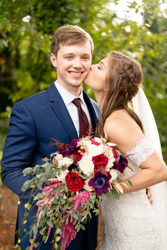 bride kisses groom's cheek while he holds her bouquet