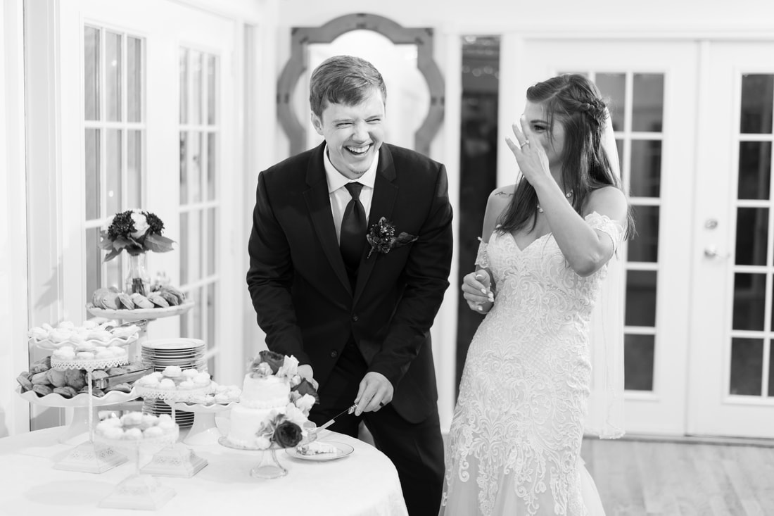 black and white photo of newlyweds laughing during cake cutting