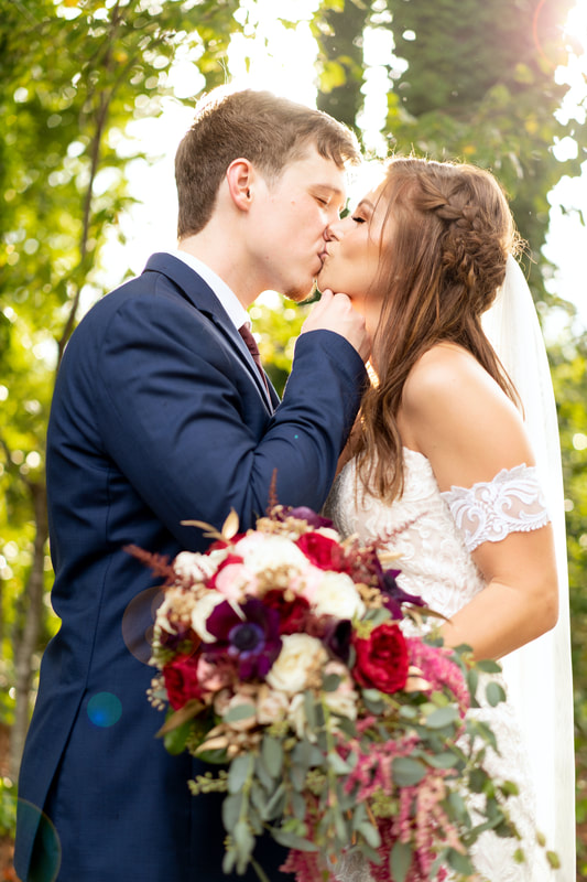 newlyweds kiss surrounded by trees with light shining behind them