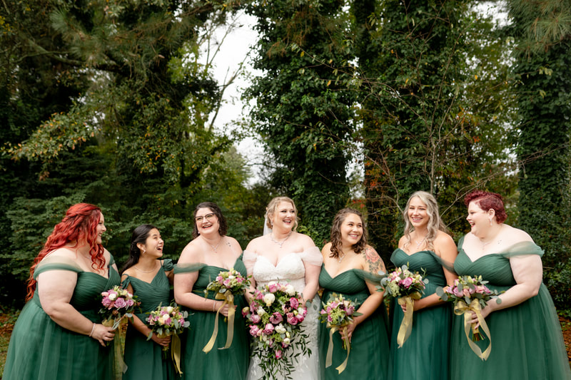 bride posing with bridesmaids in emerald dresses holding bouquets with champagne-colored ribbons