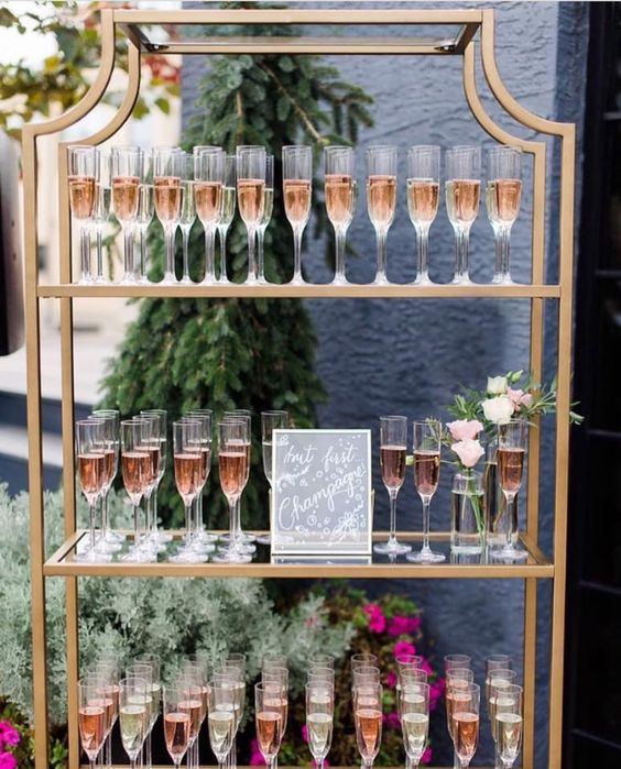 champagne flutes set on tall gold stand with sign and florals