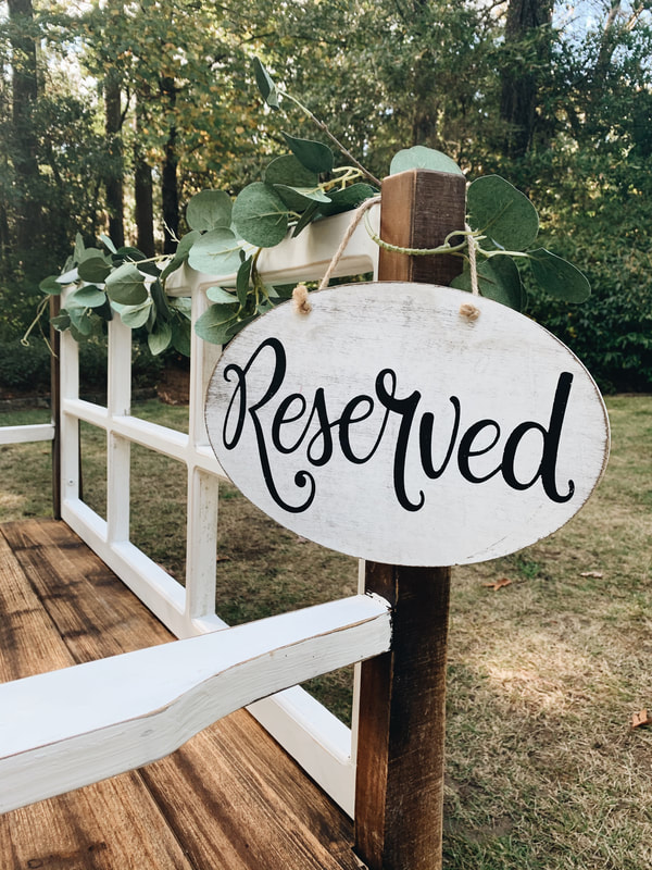 white and wood ceremony bench with greenery and reserved sign
