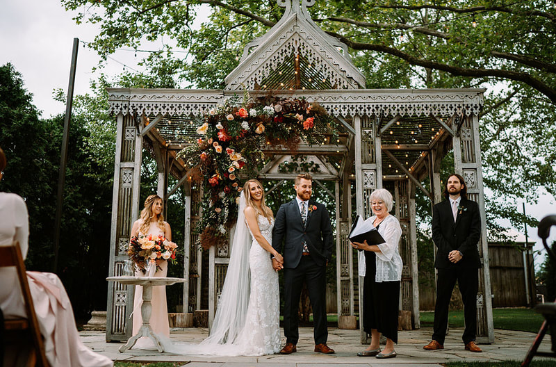 couple holding hands at floral decorated gazebo with best man and maid of honor